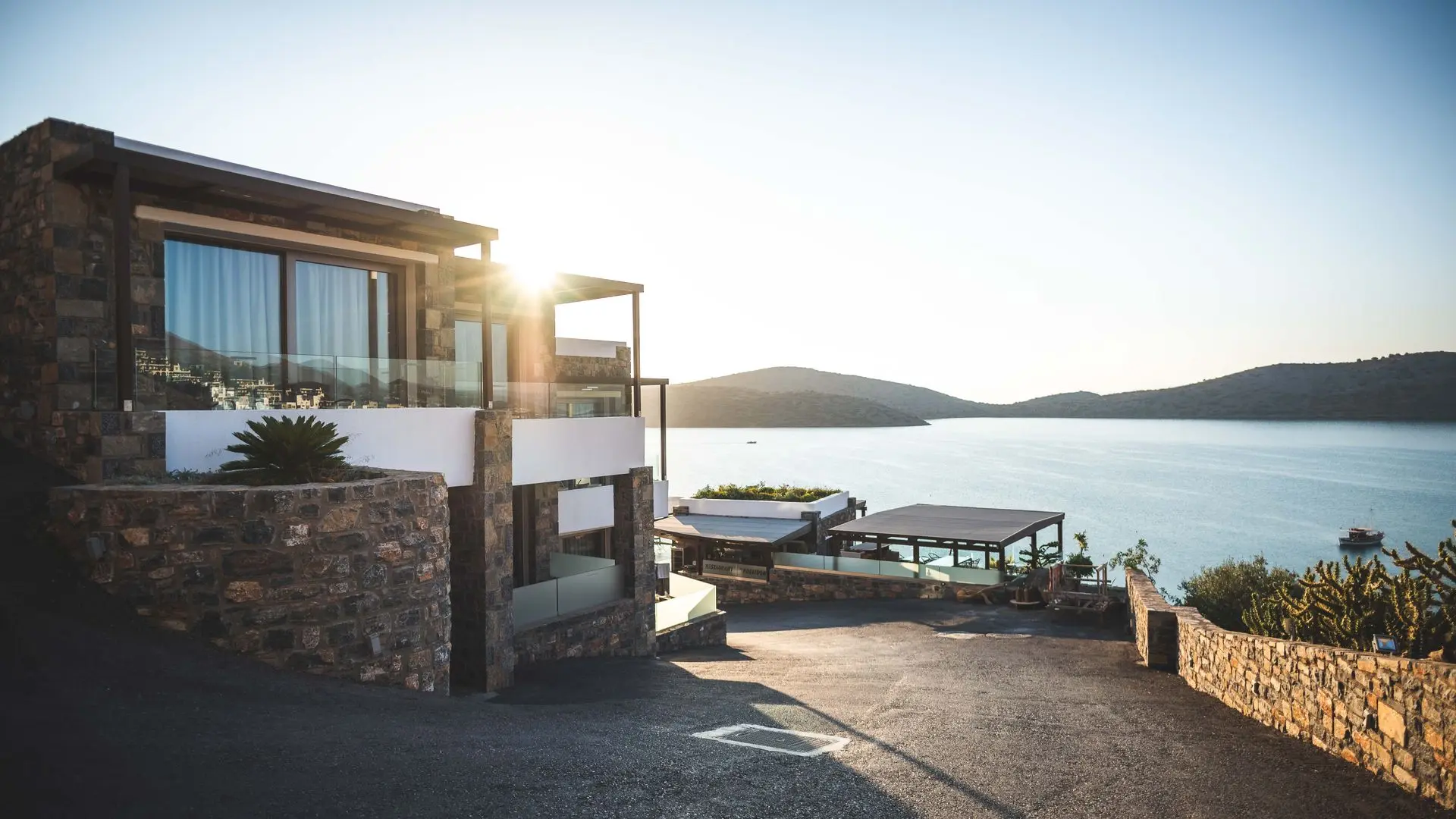 Villa de piedra de lujo sobre el mar al atardecer, con el sol reflejándose en la fachada